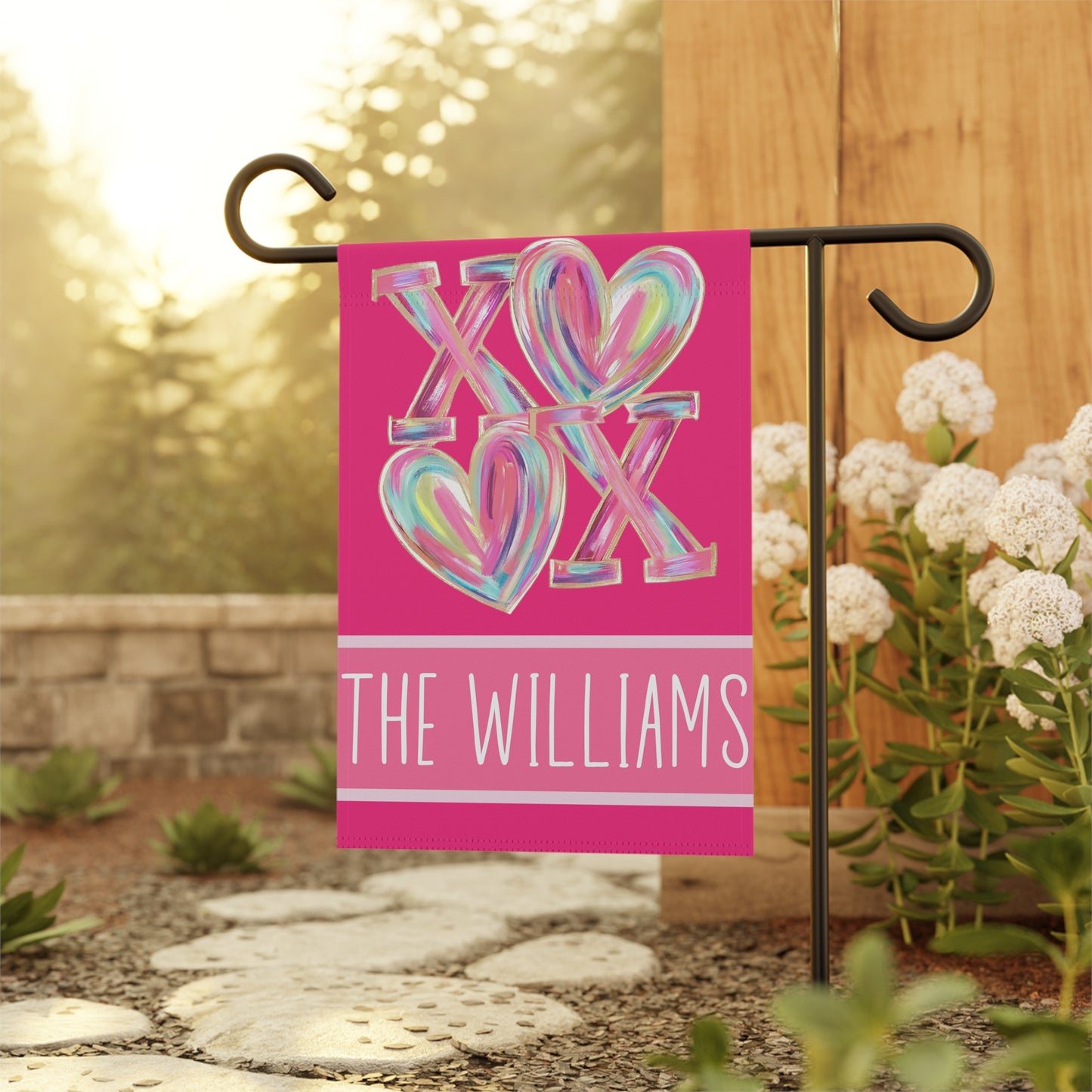 Valentines day garden flag on metal stand in green backyard, hot pink XOXO heart design with custom family name