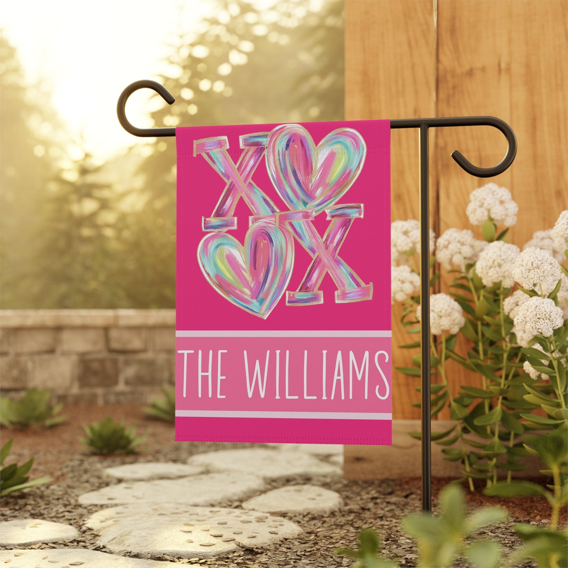 Valentines day garden flag on metal stand in green backyard, hot pink XOXO heart design with custom family name