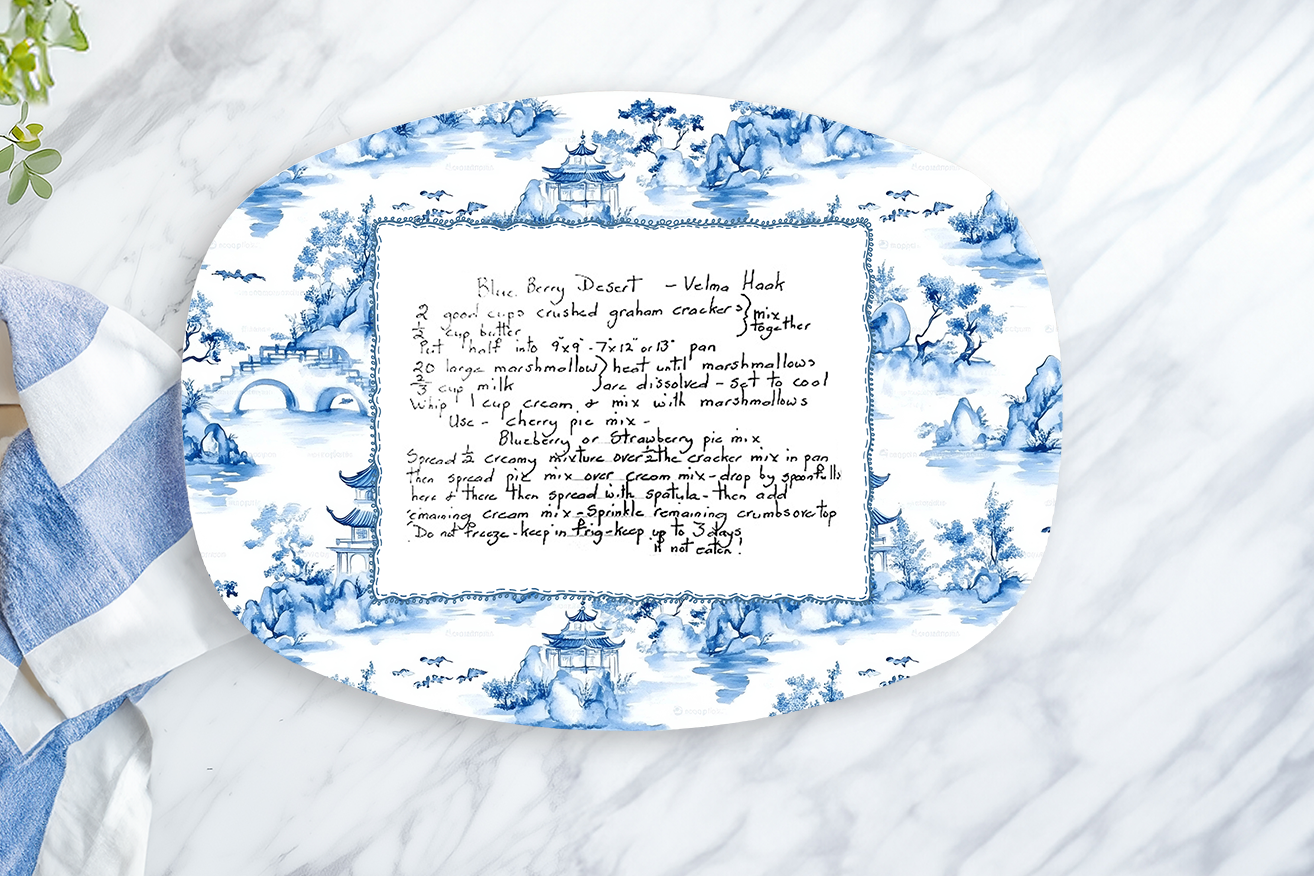 Decorative oval platter with blue floral pattern and text on a marble surface with a lemon and towel.