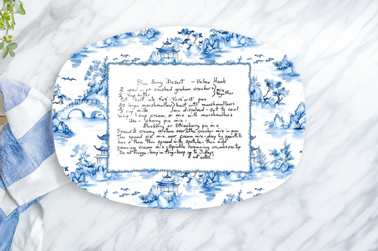 Decorative oval platter with blue floral pattern and text on a marble surface with a lemon and towel.