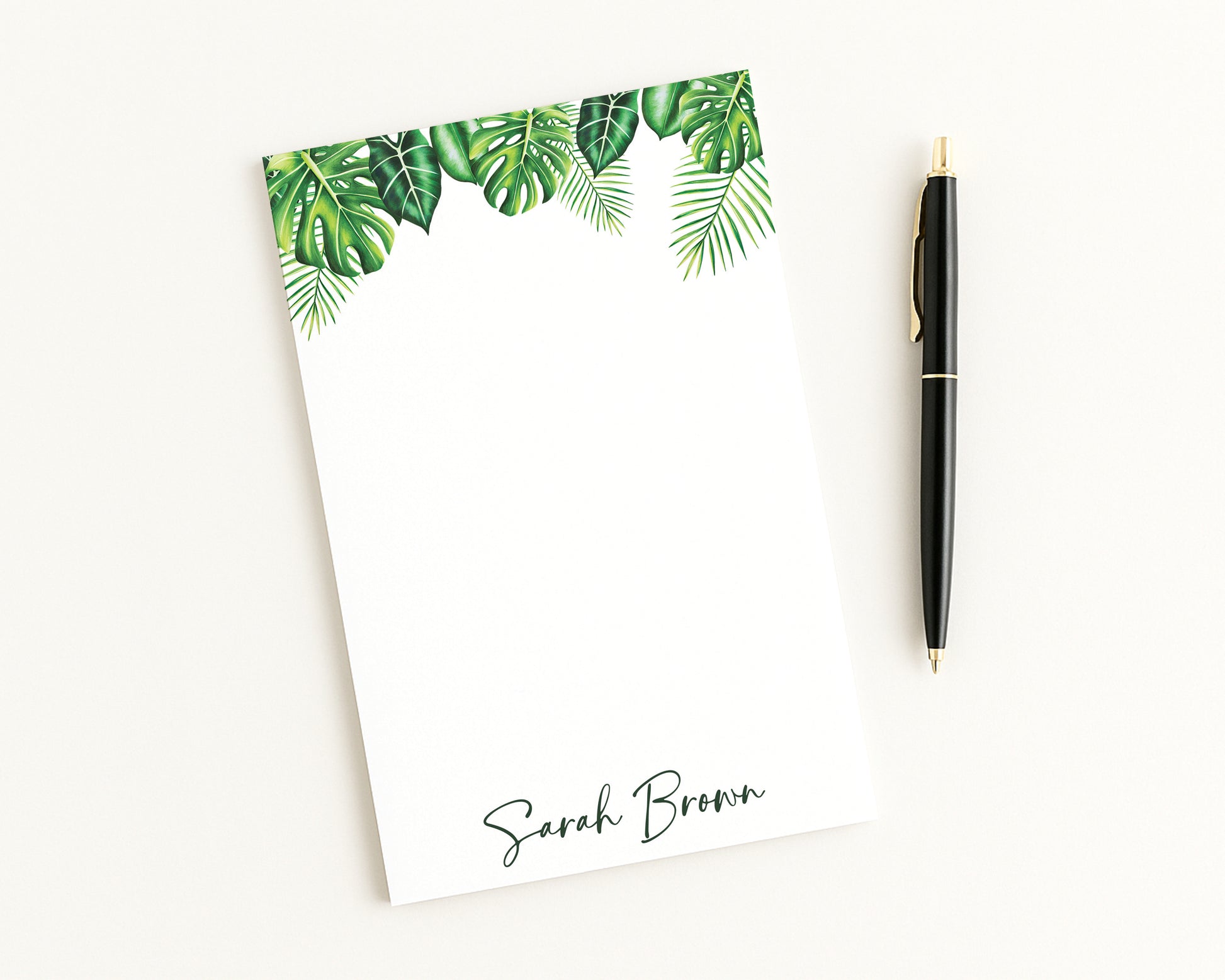 Notepad with tropical leaf design and pen on a white background