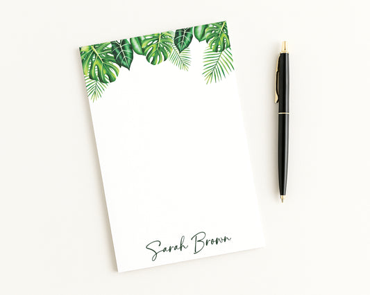 Notepad with tropical leaf design and pen on a white background