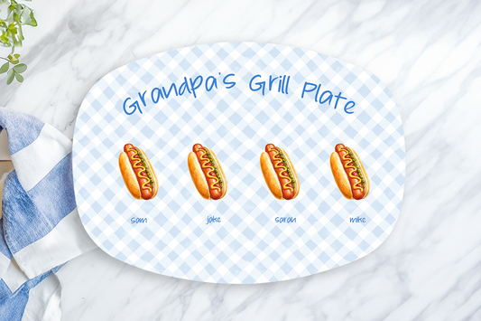 Platter with cartoon hot dogs labeled 'Granny's Grill Plate' on a marble surface with a towel and lemon.