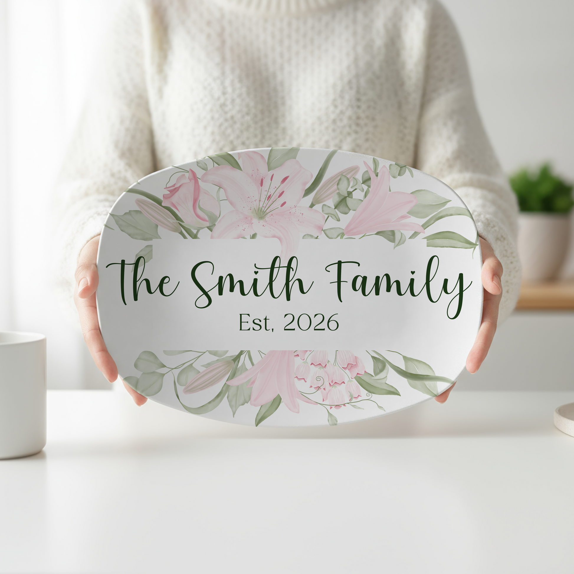 Personalized oval serving platter featuring elegant blush pink lilies, soft green botanical accents, custom family name, and optional established year. Floral serving tray perfect for weddings, housewarming gifts, entertaining, and personalized kitchen décor.