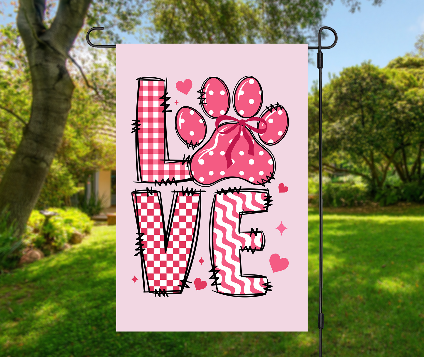 Valentines dog garden flag with pink LOVE letters and paw print with bow on light pink background, hanging on metal stand in green yard