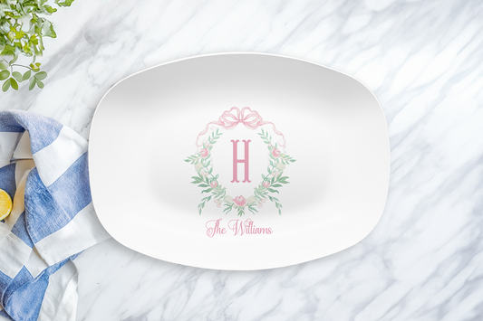 White oval platter with pink peony monogram crest and name on a marble surface