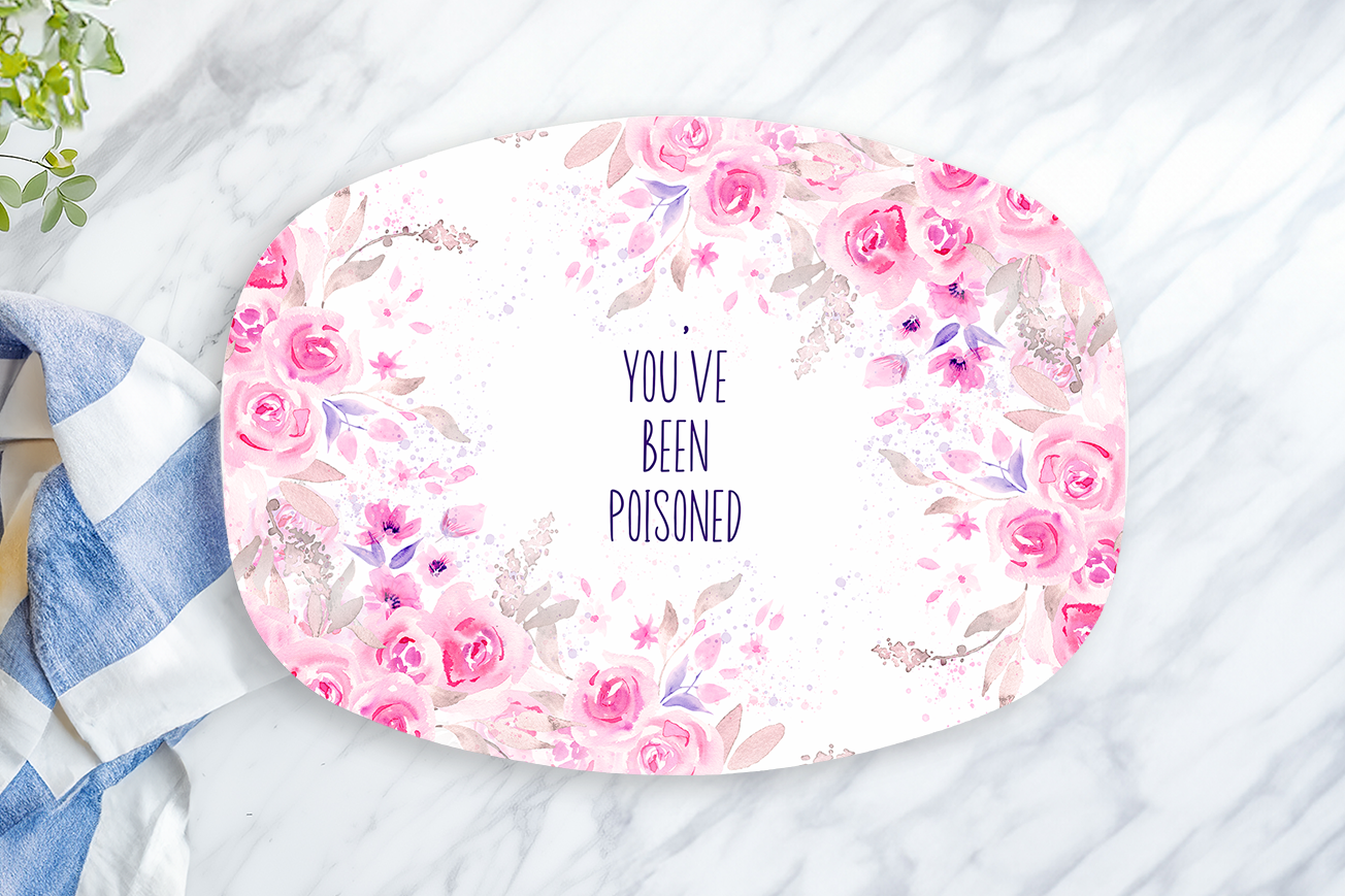 Floral plate with 'You've been poisoned' text on a marble surface with a towel and lemon.