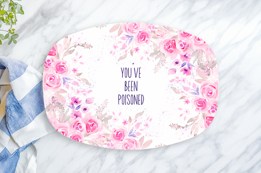 Floral plate with 'You've been poisoned' text on a marble surface with a towel and lemon.