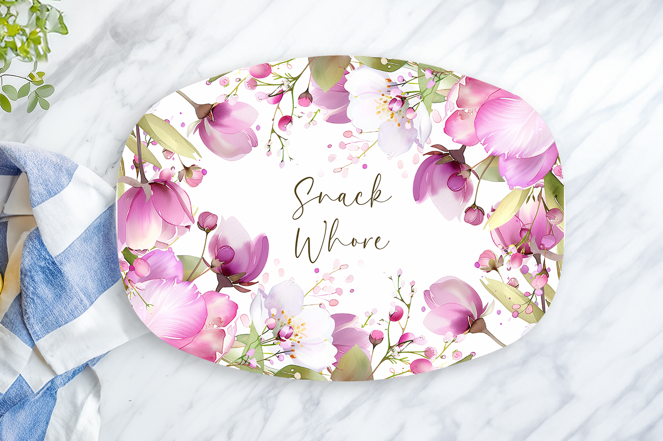 Floral-patterned plate with 'Snack Whore' text on a marble surface with a towel and lemon.