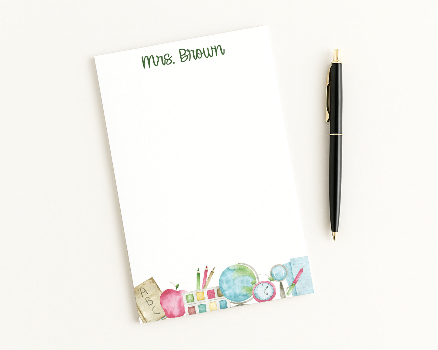 Notepad with teacher-themed design and pen on a white background