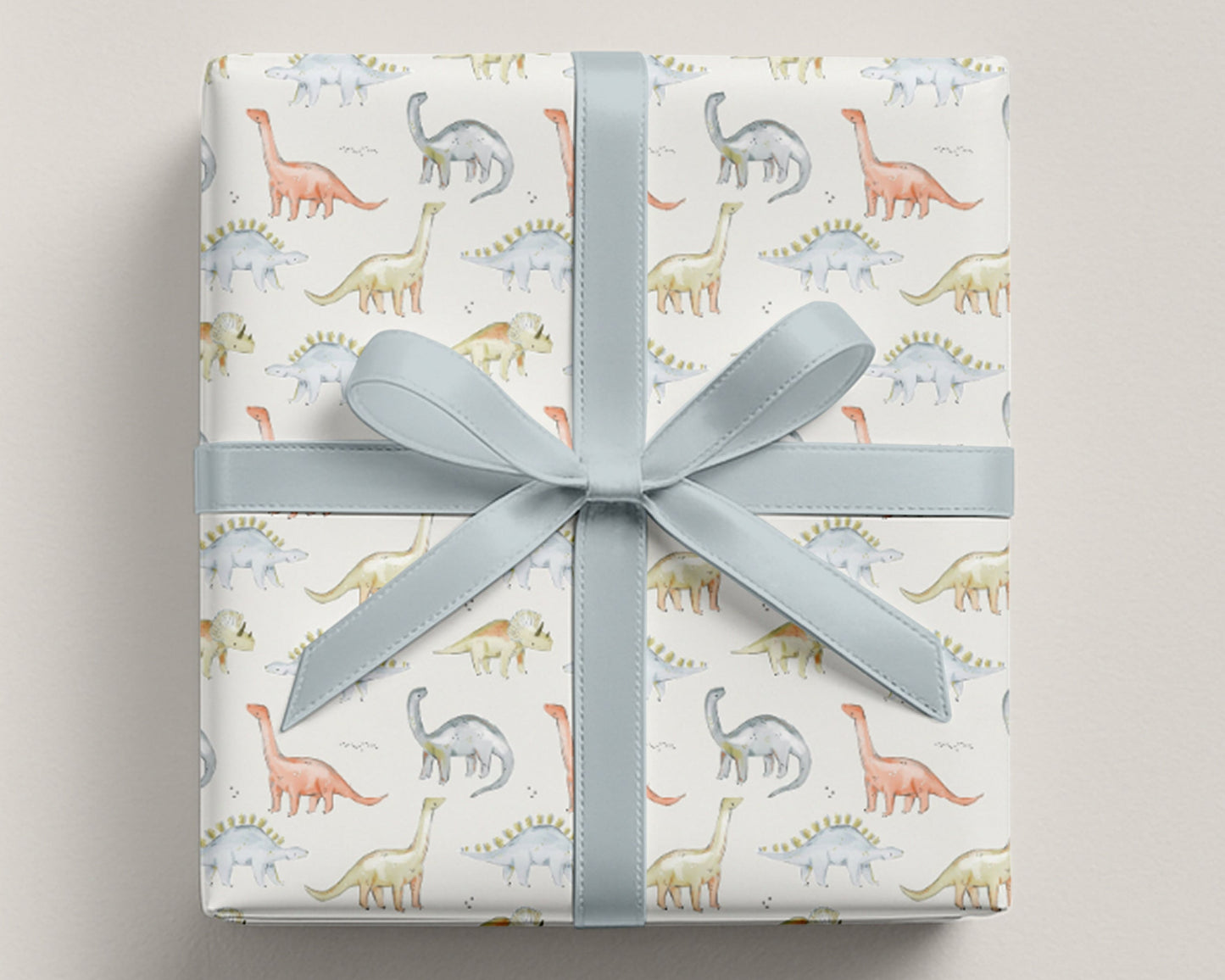 Gift box with dinosaur patterned wrapping paper on a light gray background