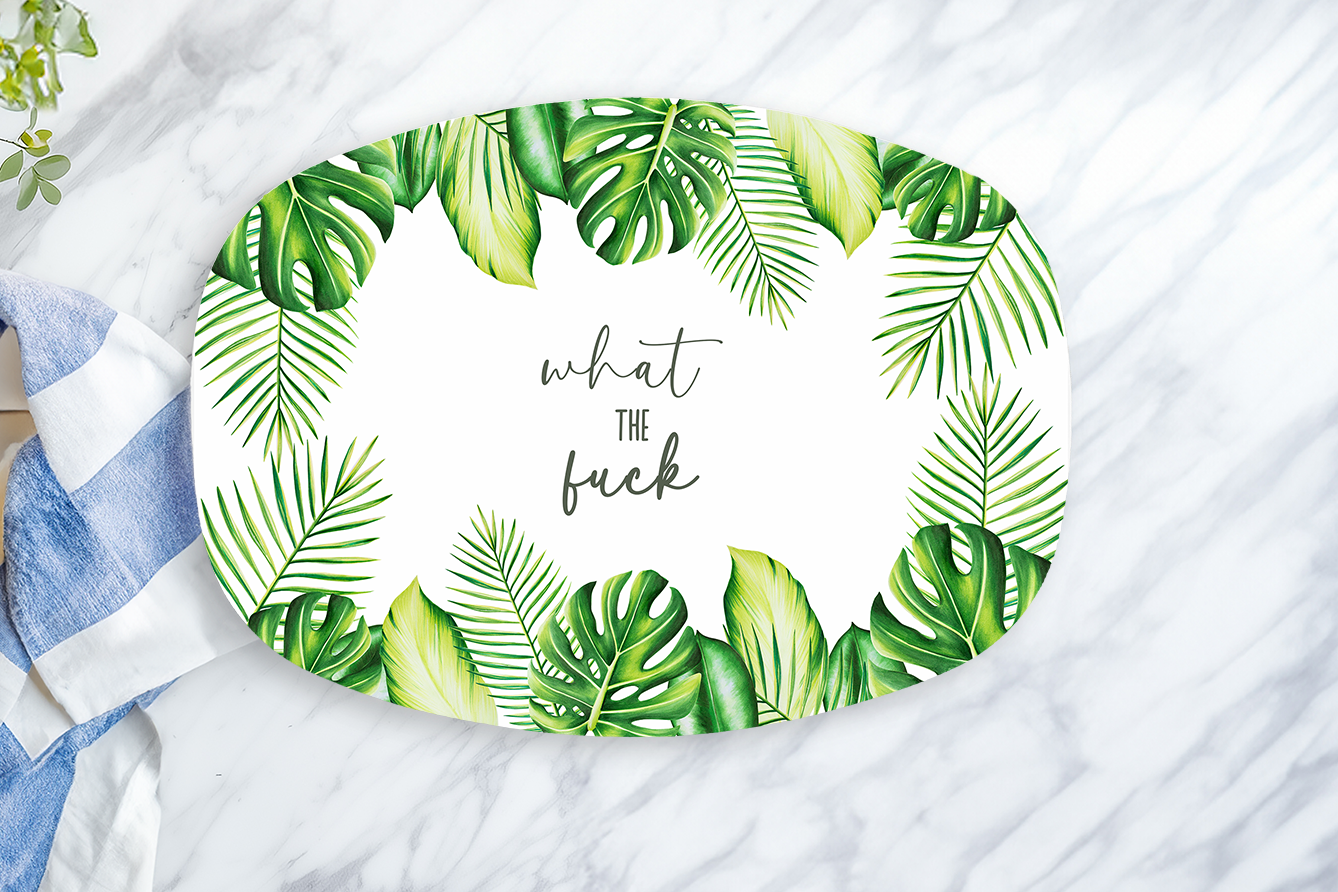 Oval plate with tropical leaf design and text on a marble surface with a towel and lemon.
